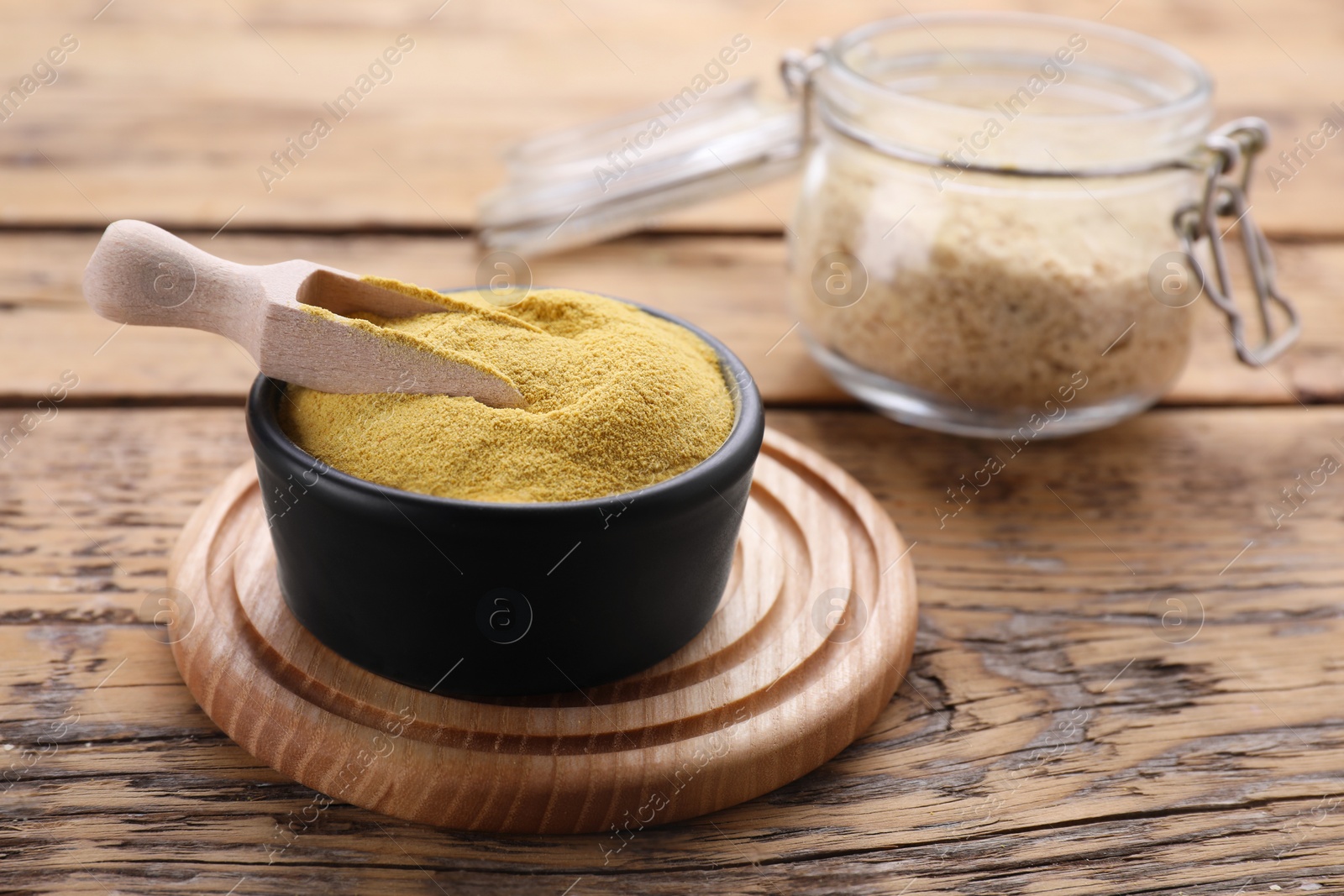 Photo of Bowl and scoop of granulated brewer`s yeast on wooden table