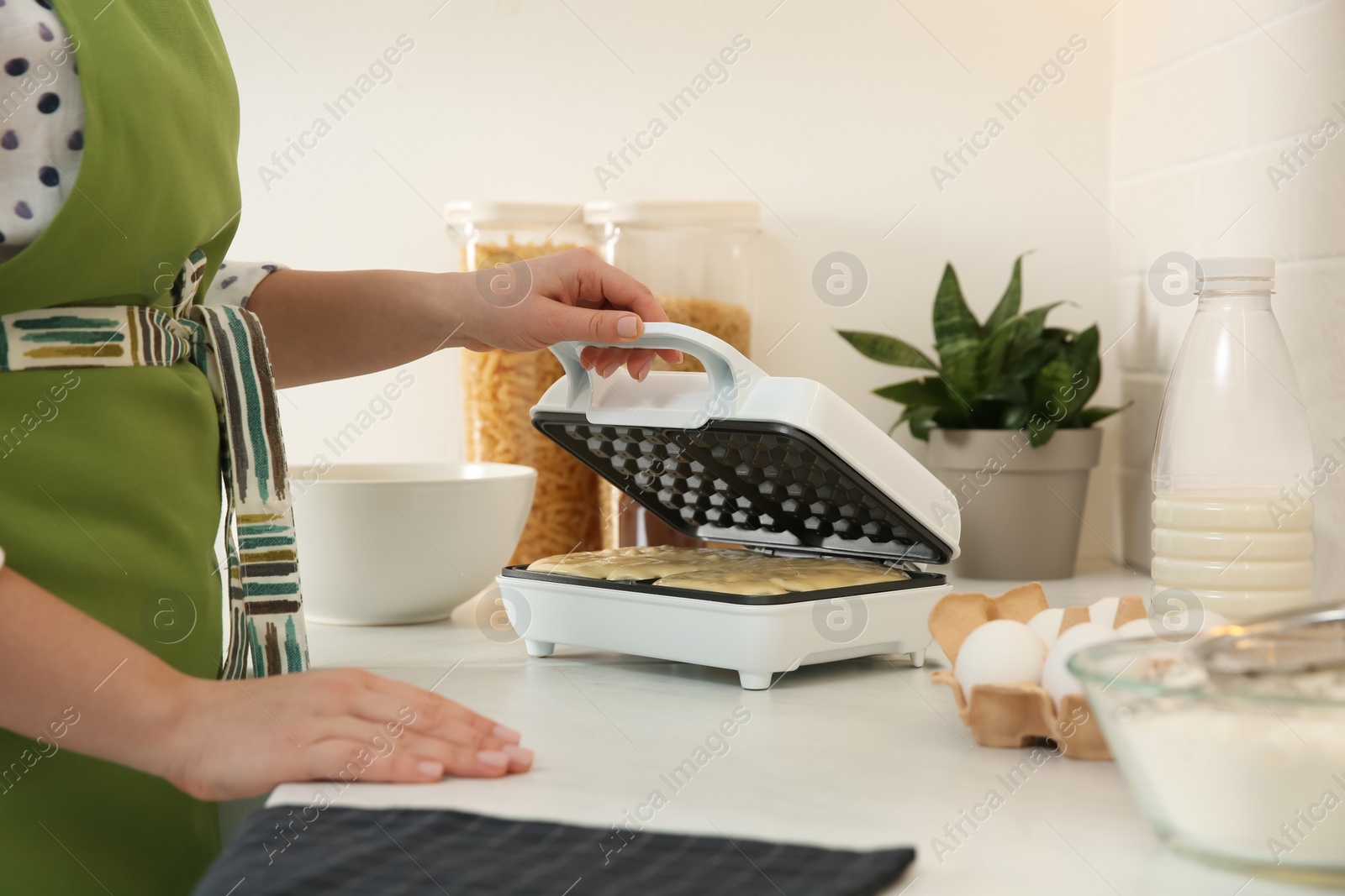 Photo of Woman closing modern Belgian waffle maker with dough in kitchen, closeup