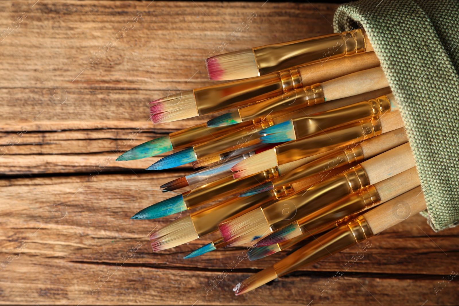 Photo of Many paintbrushes in sack on wooden table, top view