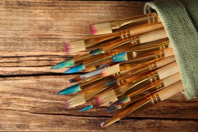 Photo of Many paintbrushes in sack on wooden table, top view
