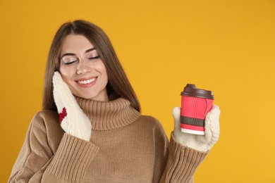 Happy beautiful woman with paper cup of mulled wine on yellow background