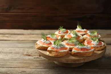 Tasty canapes with salmon, cucumber, cream cheese and dill on wooden table, space for text