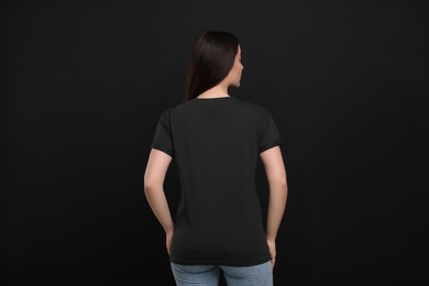 Woman wearing black t-shirt on dark background, back view