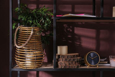 Photo of Stylish holder with burning candle, houseplant and decor on shelving unit near brown wall