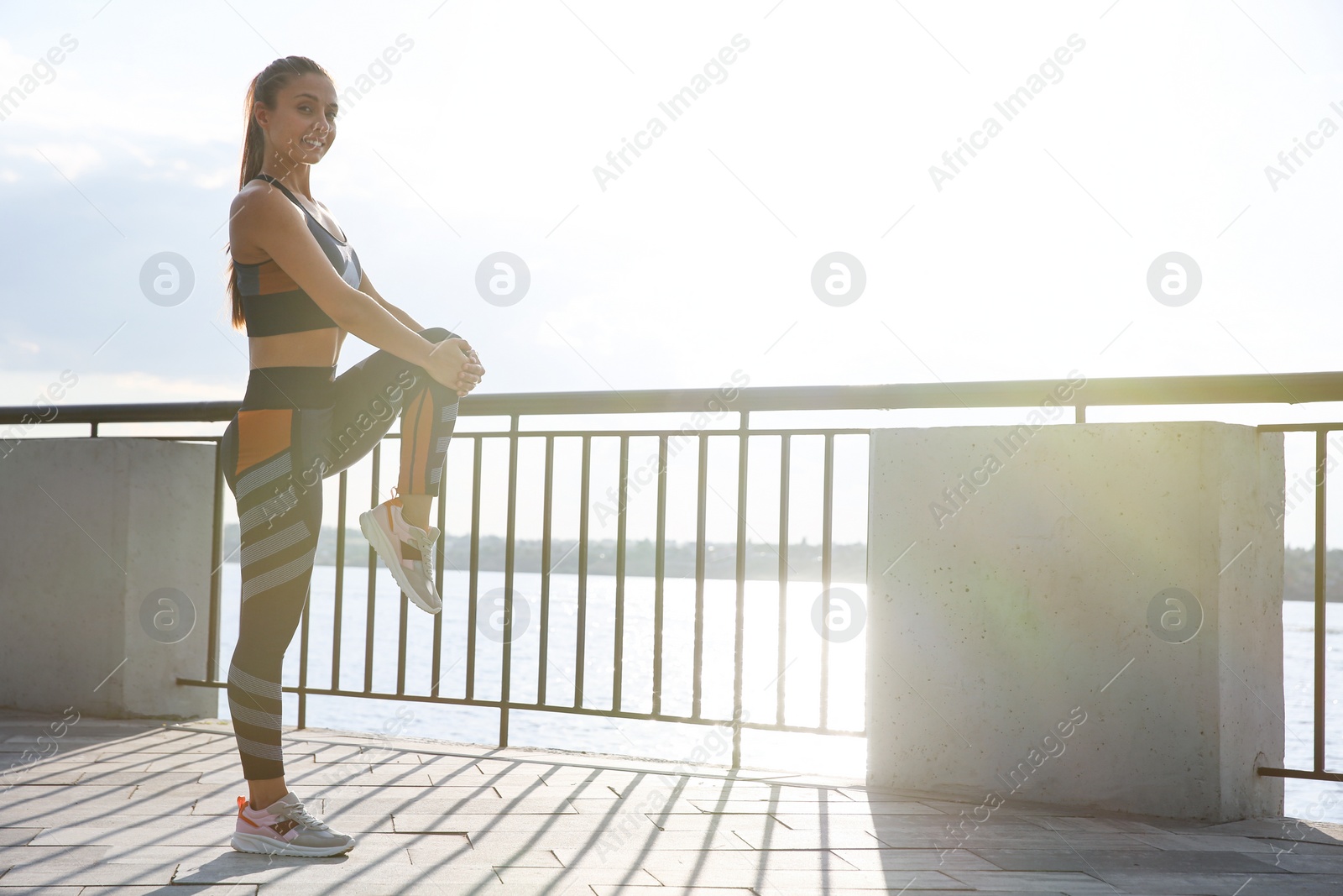 Photo of Young woman stretching on pier near river in morning. Space for text