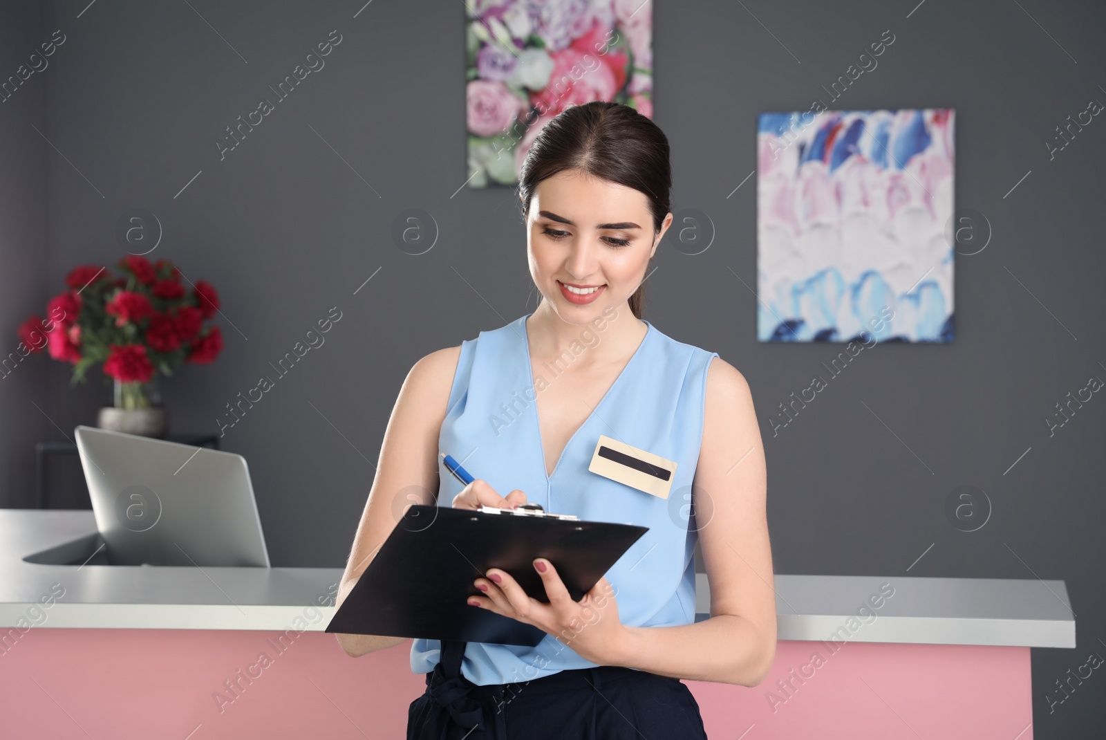 Photo of Young receptionist with clipboard at desk in beauty salon