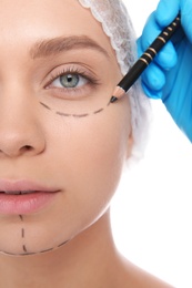 Doctor marking young woman face before cosmetic surgery on white background, closeup