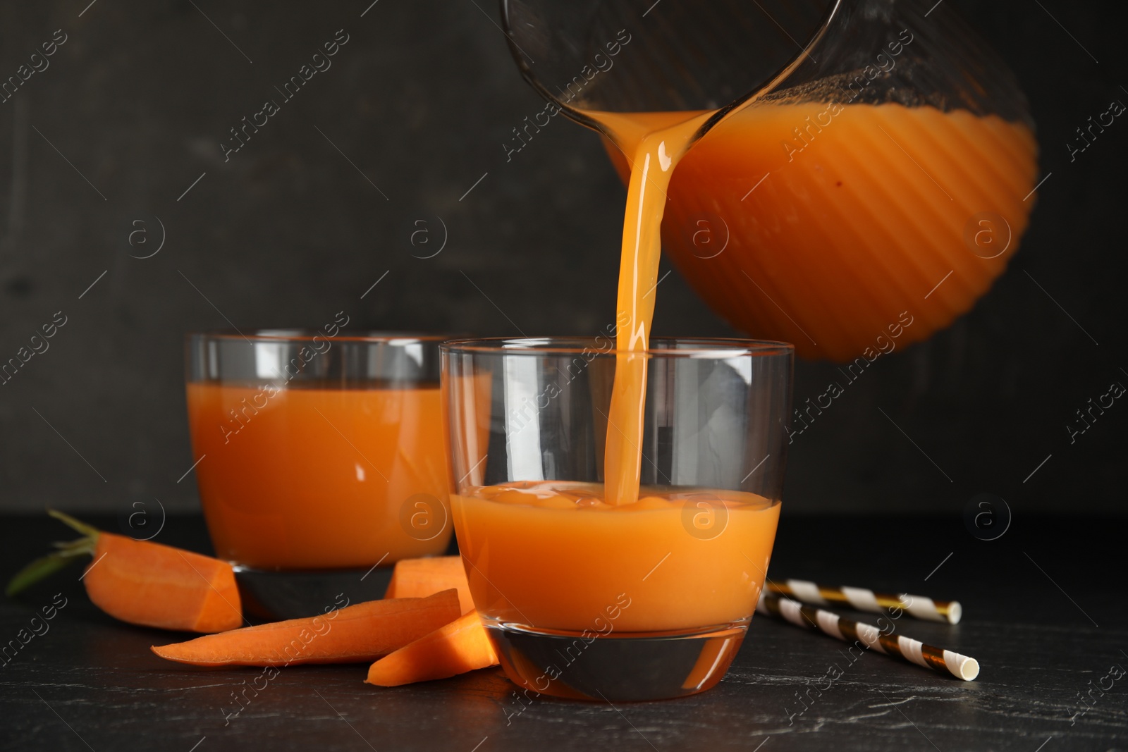 Photo of Pouring freshly made carrot juice into glass on black table