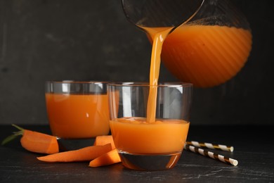 Photo of Pouring freshly made carrot juice into glass on black table