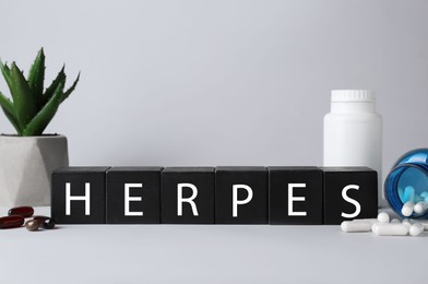 Word Herpes made of black wooden cubes, different pills and houseplant on grey table