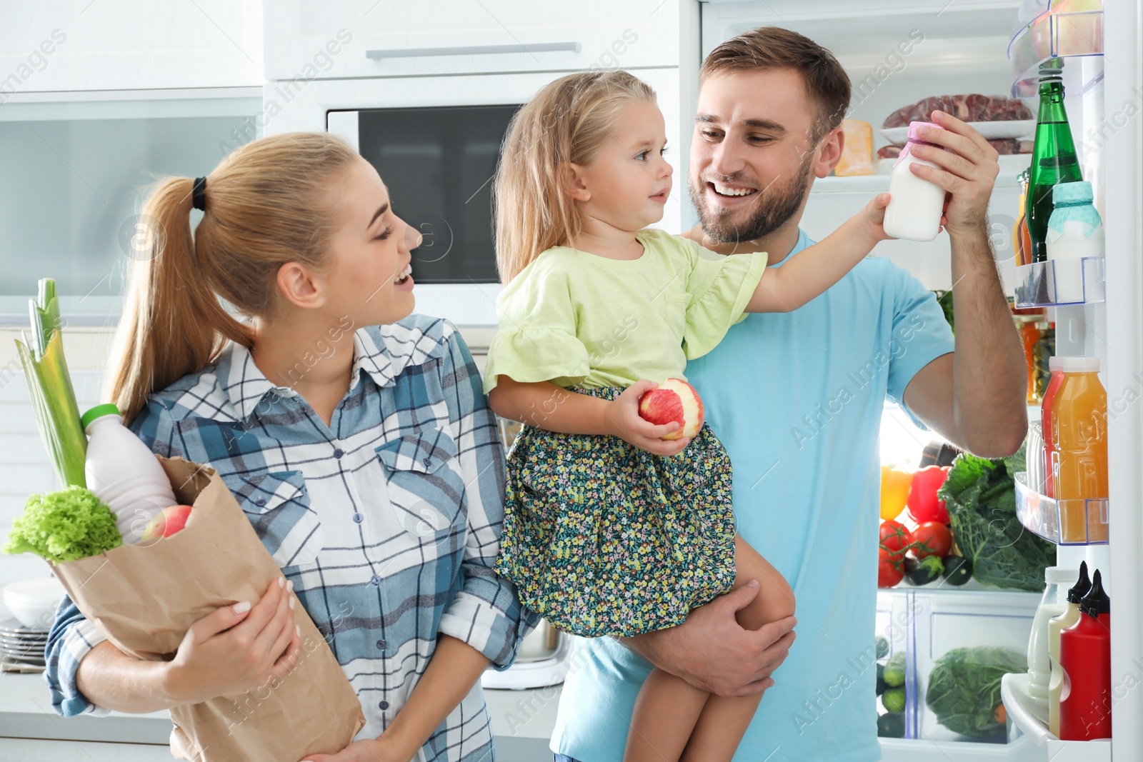 Photo of Happy family with products near refrigerator in kitchen