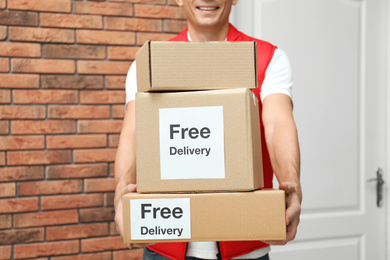 Photo of Courier holding parcels with stickers Free Delivery indoors, closeup