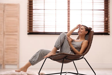 Young woman relaxing in chair near window with blinds at home. Space for text