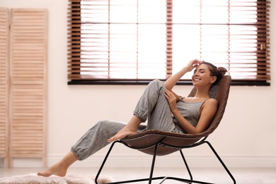 Photo of Young woman relaxing in chair near window with blinds at home. Space for text