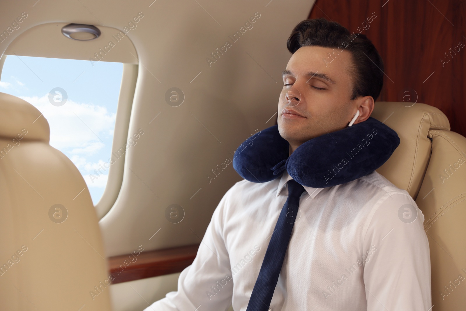 Photo of Young man with travel pillow resting while listening to music in airplane during flight