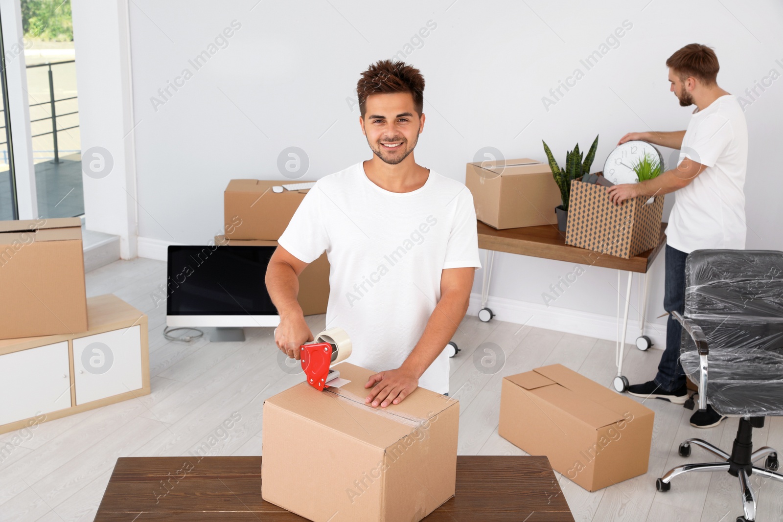 Photo of Young worker packing box and his colleague in office. Moving service