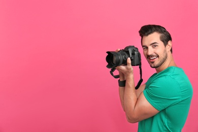 Young photographer with professional camera on pink background. Space for text