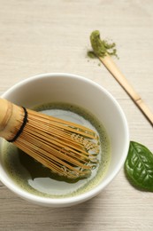 Photo of Cup of fresh green matcha tea with bamboo whisk and spoon on wooden table, closeup