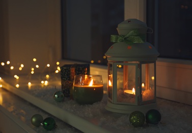 Photo of Beautiful Christmas lantern and other decorations on snowy window sill at night