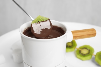 Photo of Dipping kiwi into fondue pot with chocolate on white table