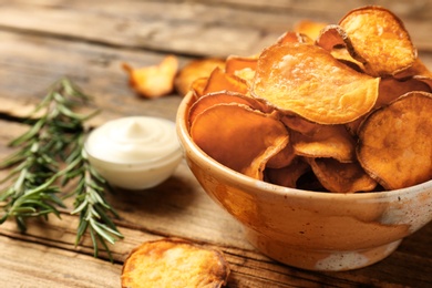 Photo of Delicious sweet potato chips in bowl, rosemary and sauce on table. Space for text