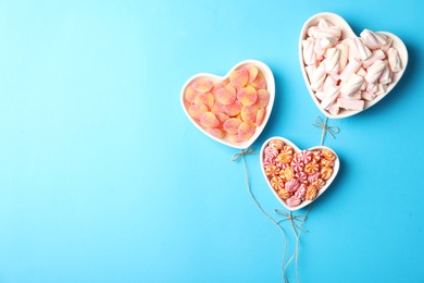 Twine near heart shaped bowls full of sweets imitating balloons on light blue background, top view. Space for text