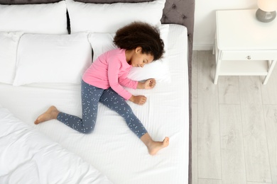 Cute little African-American girl sleeping in bed, top view