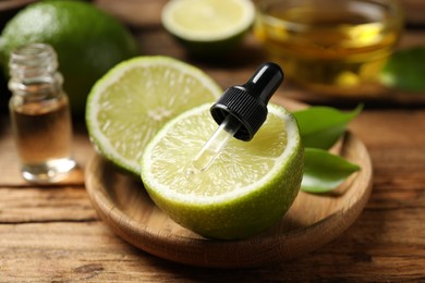 Photo of Dropper with lime essential oil and cut citrus fruit on wooden table