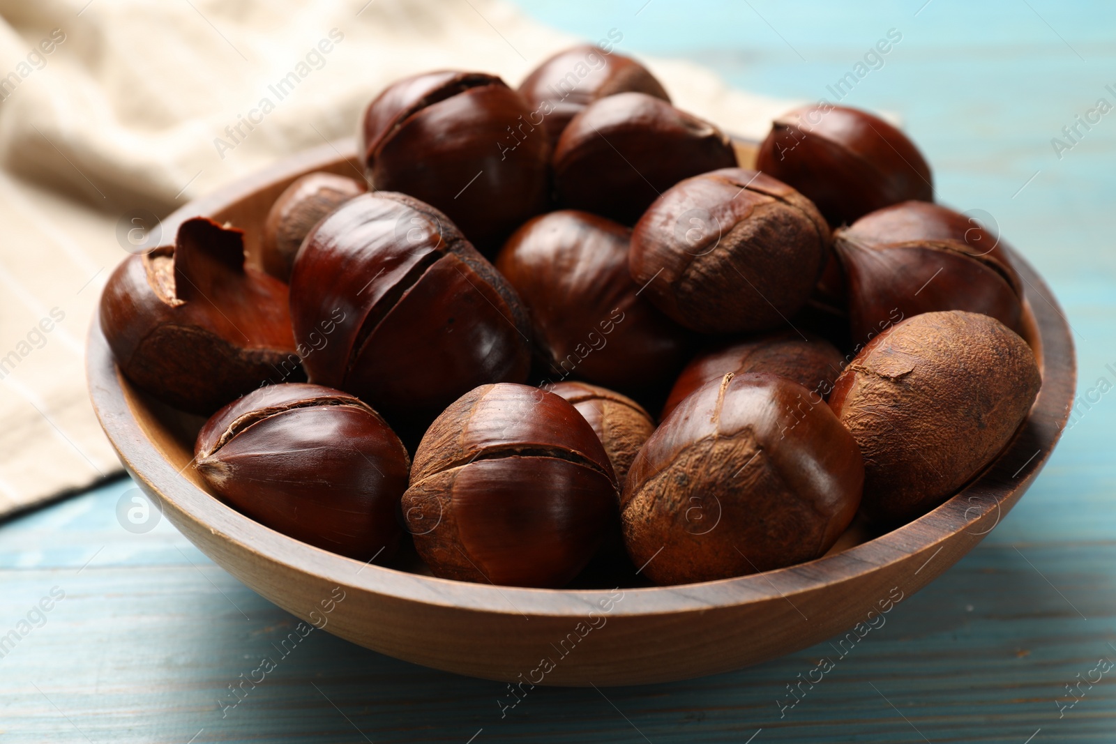 Photo of Fresh edible sweet chestnuts in bowl on light blue wooden table