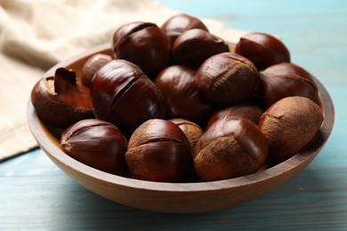 Photo of Fresh edible sweet chestnuts in bowl on light blue wooden table