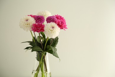 Photo of Bouquet of beautiful Dahlia flowers in vase near white wall, space for text