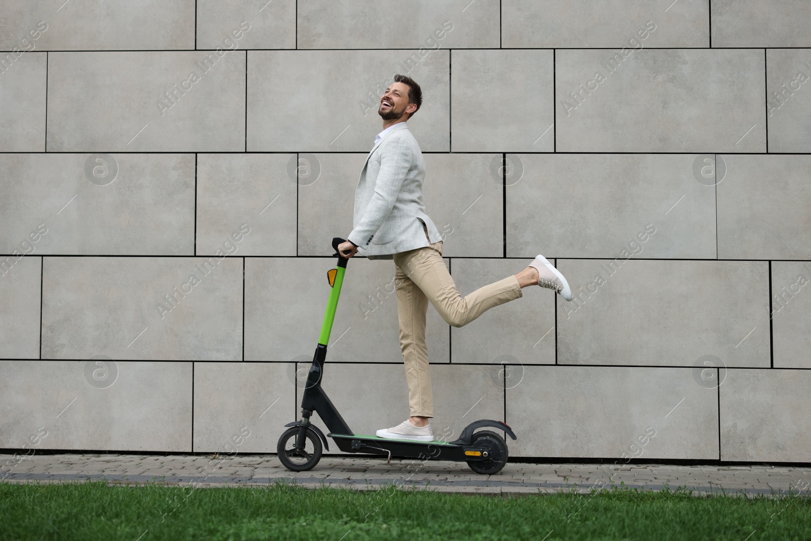 Photo of Businessman riding modern kick scooter near grey stone wall outdoors