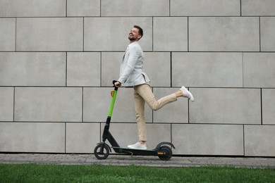 Businessman riding modern kick scooter near grey stone wall outdoors