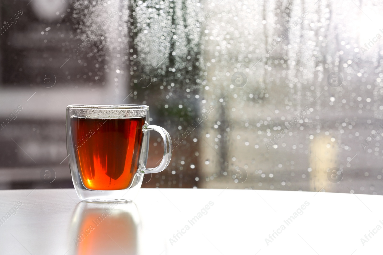 Photo of Cup of fresh hot tea on wooden window sill against glass with rain drops. Space for text