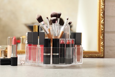 Photo of Lipstick holder with different makeup products on dressing table near mirror