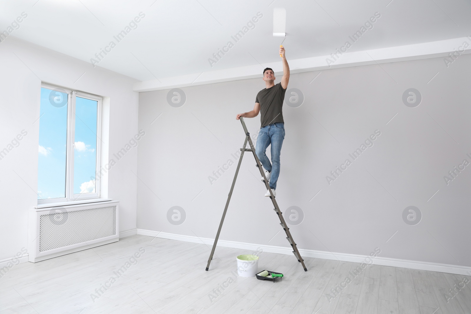 Photo of Man painting ceiling with roller on step ladder in room