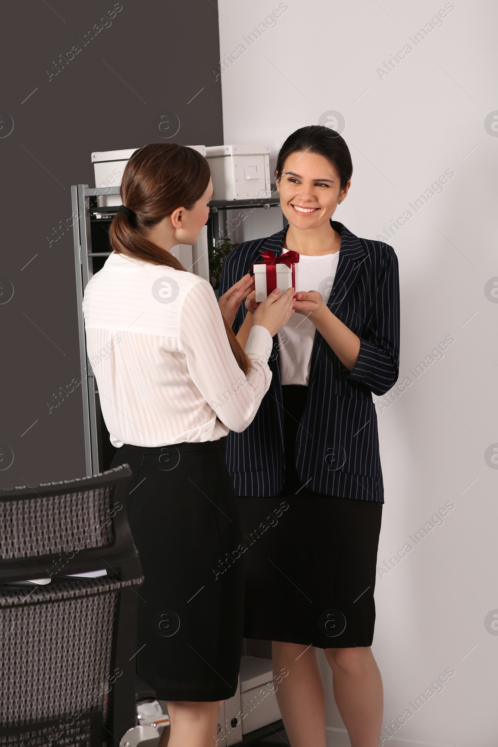 Photo of Woman presenting gift to her colleague in office