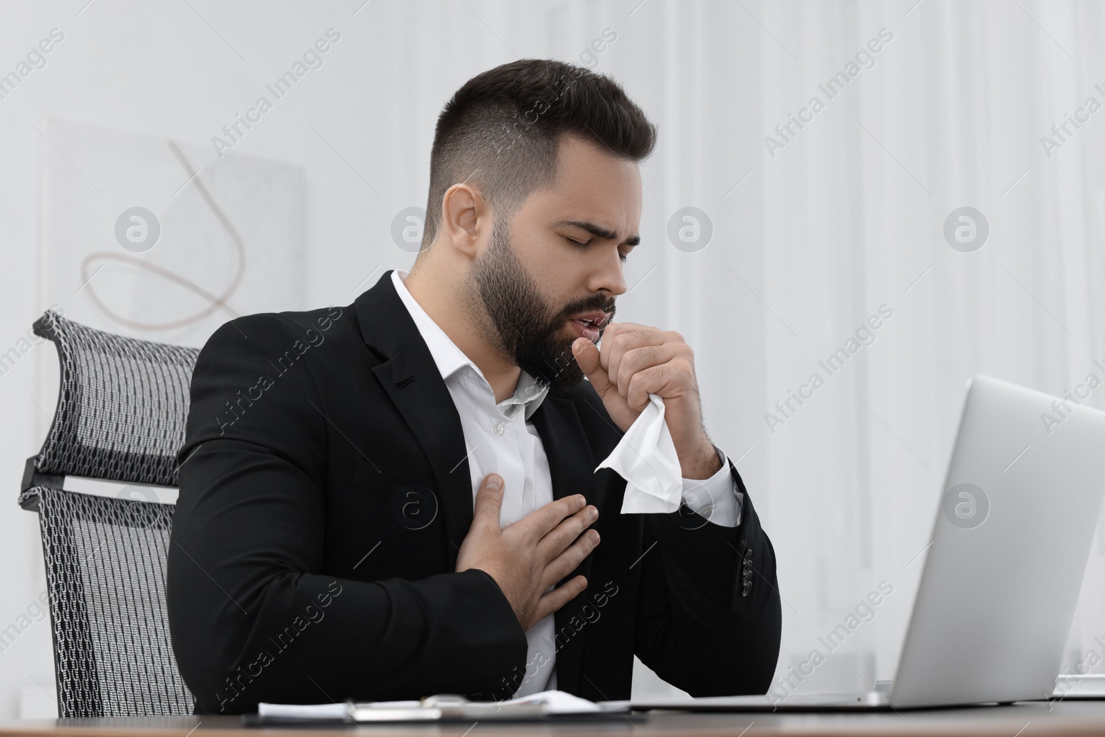 Photo of Sick man with tissue coughing at workplace in office