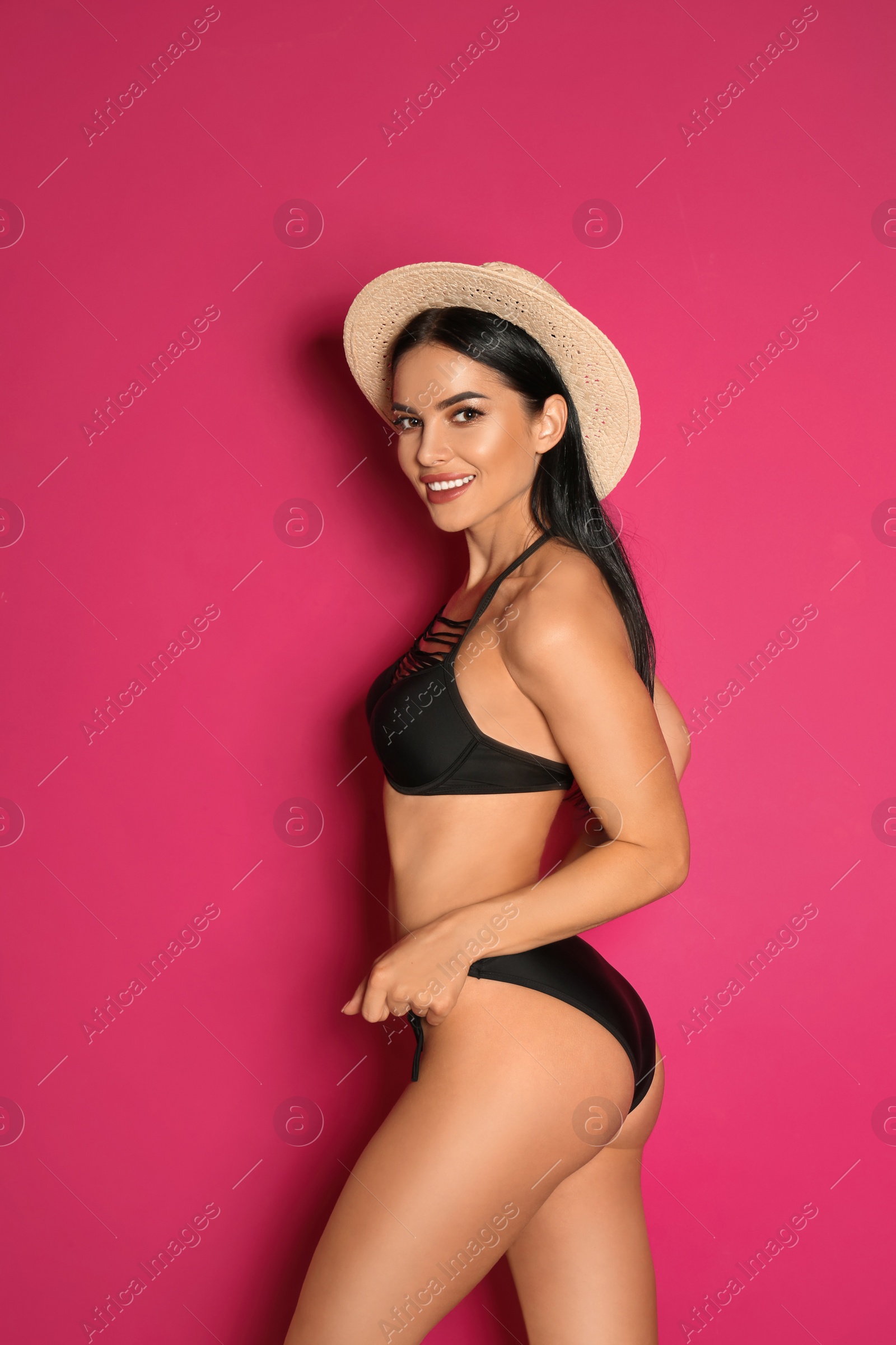 Photo of Beautiful young woman in black bikini with hat on pink background