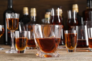 Photo of Different delicious liqueurs in glasses and bottles on wooden table