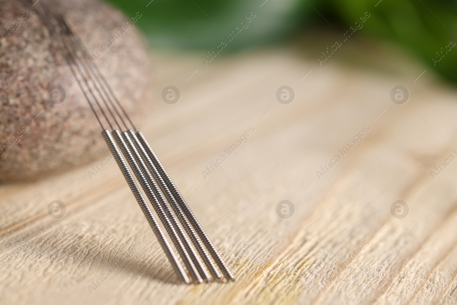 Photo of Acupuncture needles and spa stone on wooden table, closeup. Space for text