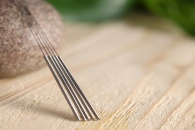 Photo of Acupuncture needles and spa stone on wooden table, closeup. Space for text