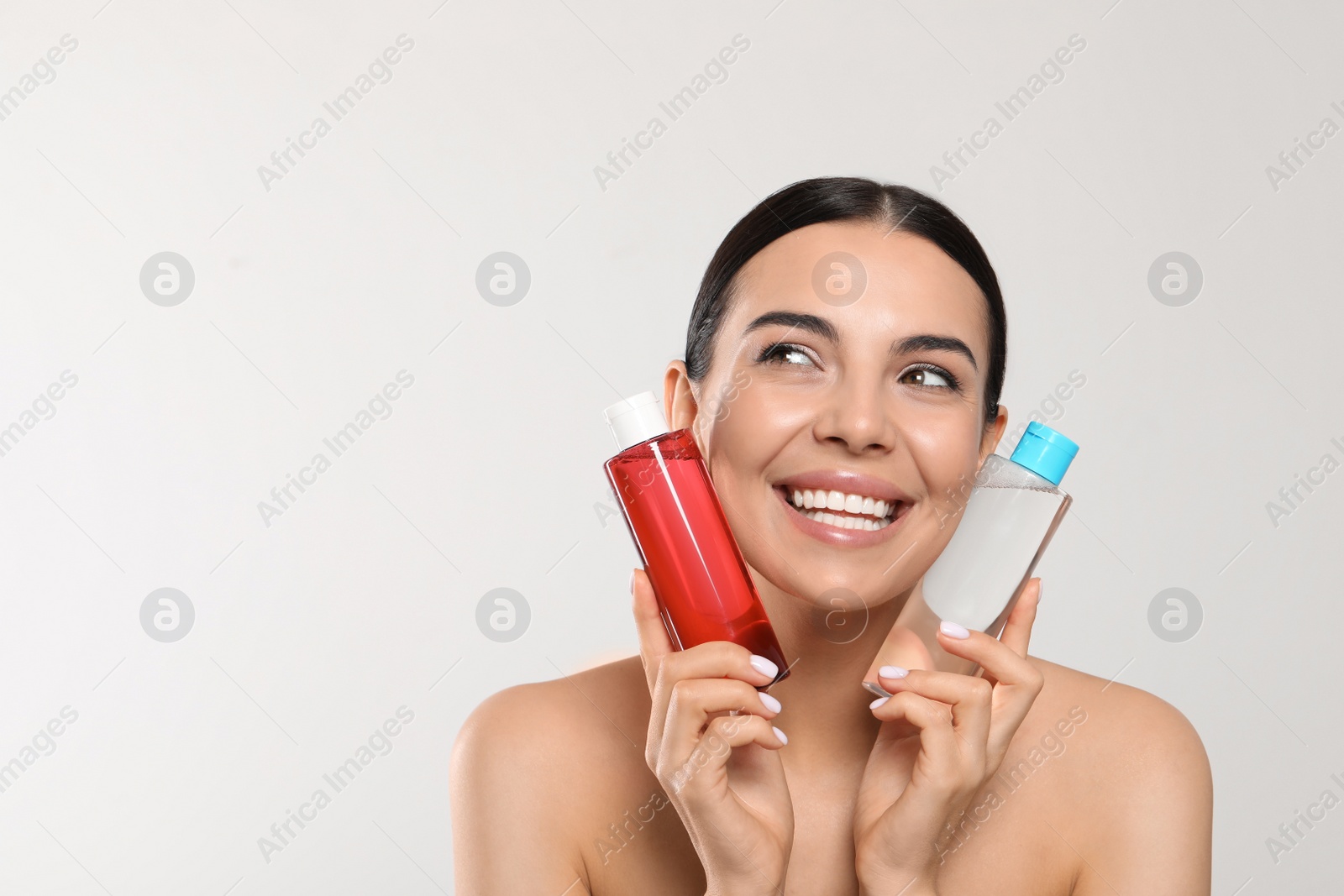 Photo of Young woman with bottles of micellar water on light grey background, space for text