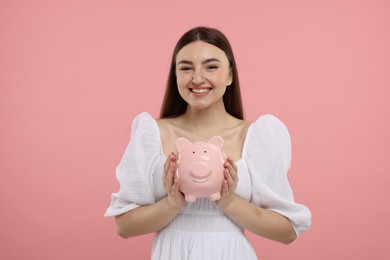 Photo of Happy woman with piggy bank on pink background