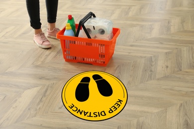 Image of Woman near sign KEEP DISTANCE in supermarket. Coronavirus pandemic