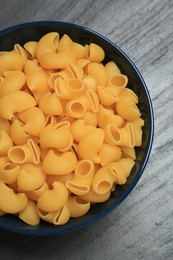 Photo of Raw macaroni pasta in bowl on grey table, top view