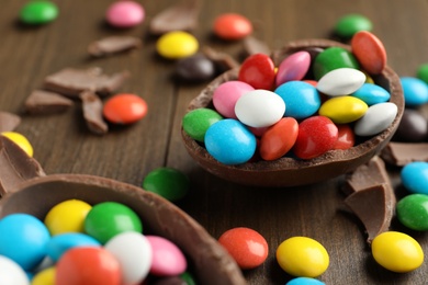 Photo of Broken chocolate egg and colorful candies on wooden table, closeup