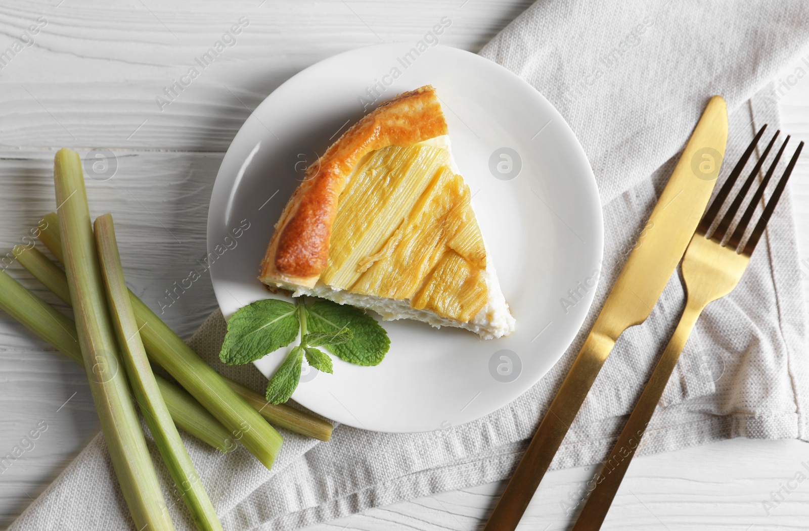 Photo of Piece of freshly baked rhubarb pie, stalks and cutlery on white wooden table, flat lay