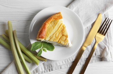 Photo of Piece of freshly baked rhubarb pie, stalks and cutlery on white wooden table, flat lay