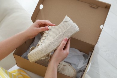Photo of Woman with canvas shoes and box on sofa, closeup